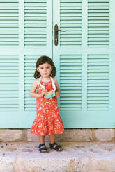 Porträt eines kleinen Mädchens mit hölzerner Spielzeugkamera im roten Kleid mit Blumenmuster - GEMF03116