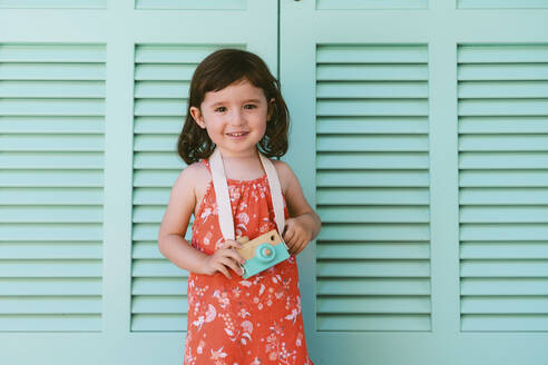 Porträt eines lächelnden kleinen Mädchens mit Holzspielzeugkamera - GEMF03117