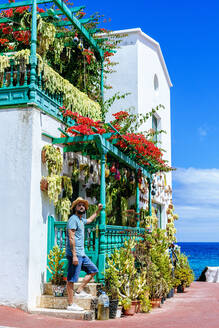 Man with hat next to house full of flowers, Lanzarote, Canary Islands, Spain - KIJF02629
