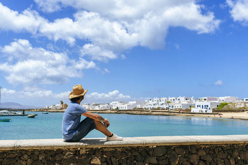 Man sitting on wall looking towards Caleta de Sebo, La Graciosa, Canary Islands, Spain - KIJF02644