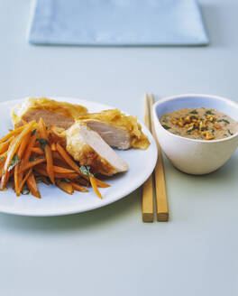 Close-up of chicken breast with carrots and peanut sauce on table - PPXF00261