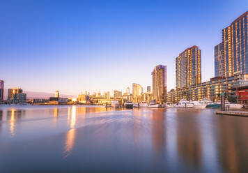 Beleuchtete Gebäude am Fluss in den Melbourne Docklands vor blauem Himmel in der Abenddämmerung, Victoria, Australien - SMAF01316