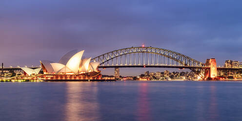 Beleuchtete Sydney Harbor Bridge über dem Fluss gegen den Himmel in der Abenddämmerung, Australien - SMA01325