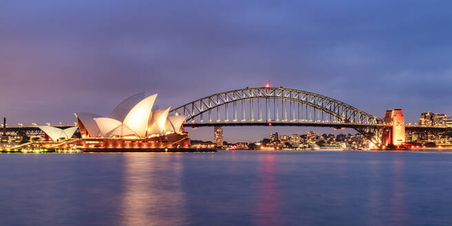 Beleuchtete Sydney Harbor Bridge über dem Fluss gegen den Himmel in der Abenddämmerung, Australien - SMA01325