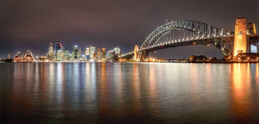 Panoramic shot of illuminated Sydney Harbor Bridge over river against sky at night, Sydney, Australia - SMAF01330