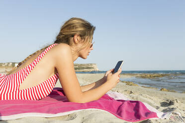 Junge Frau benutzt Smartphone am Strand - JPTF00260