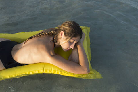 Young woman lying on yellow airbed and sleeping stock photo