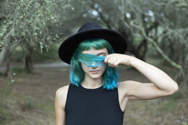 Porträt einer jungen Frau mit gefärbten blauen und grünen Haaren und schwarzem Hut an einem regnerischen Tag - JPTF00274