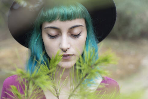 Porträt einer jungen Frau mit blau und grün gefärbtem Haar und Nasenpiercing in der Natur - JPTF00280