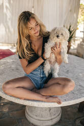 Schöne junge Frau sitzt auf einem Tisch im Freien und hält einen Hund - ACPF00602