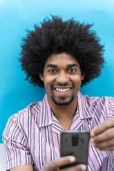 Smiling young man using smartphone, blue blackground - AFVF03807