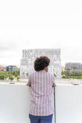 Rückansicht eines jungen Hipsters auf einem Aussichtspunkt mit Blick auf ein modernes Gebäude, Barcelona, Spanien - AFVF03817