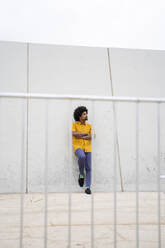 Junger Hipster in gelbem Hemd, seitwärts blickend, an eine weiße Wand gelehnt - AFVF03833