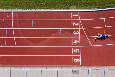 Aerial view of a young female athlete lying on a tartan track after crossing the finishing line - STSF02194