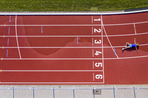 Luftaufnahme einer jungen Athletin, die auf einer Tartanbahn liegt, nachdem sie die Ziellinie überquert hat - STSF02194