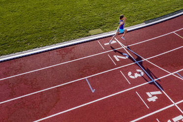 Aerial view of a running young female athlete on a tartan track crossing finishing line - STSF02197