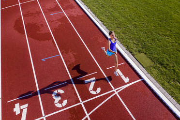 Aerial view of a running young female athlete on a tartan track crossing finishing line - STSF02198