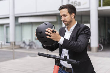 Geschäftsmann mit E-Scooter in der Stadt setzt Helm auf - DIGF08069