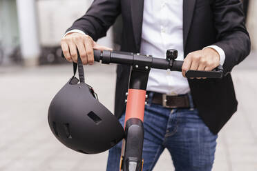 Nahaufnahme eines Geschäftsmannes mit E-Roller und Helm in der Stadt - DIGF08070