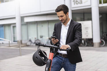 Businessman with e-scooter using cell phone in the city - DIGF08071