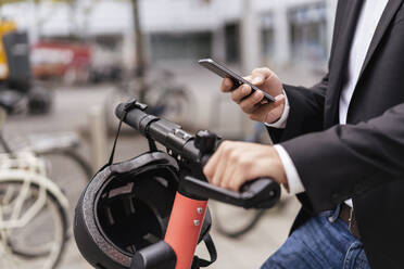 Nahaufnahme eines Geschäftsmannes mit E-Scooter, der in der Stadt ein Mobiltelefon benutzt - DIGF08072