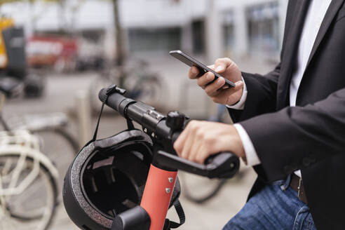 Close-up of businessman with e-scooter using cell phone in the city - DIGF08072