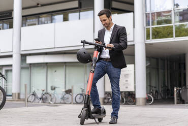 Geschäftsmann mit E-Scooter beim Telefonieren in der Stadt - DIGF08073