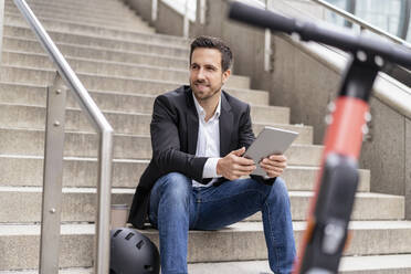 Businessman with e-scooter using tablet in the city - DIGF08077