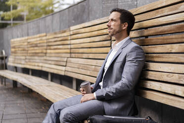 Relaxed businessman sitting on wooden bench in the city - DIGF08084