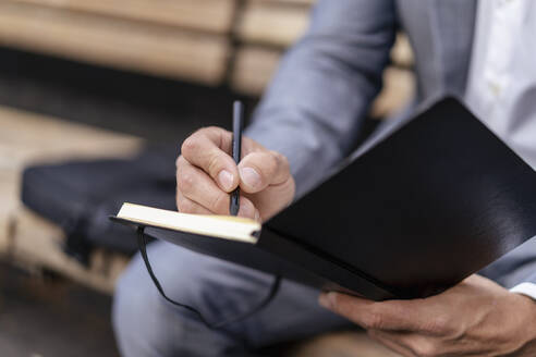 Close-up of businessman writing into notebook - DIGF08088