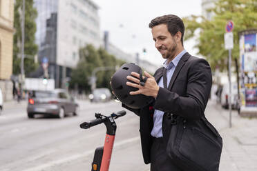 Geschäftsmann mit E-Scooter in der Stadt setzt Helm auf - DIGF08119