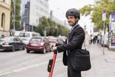 Lächelnder Geschäftsmann mit E-Scooter in der Stadt - DIGF08120