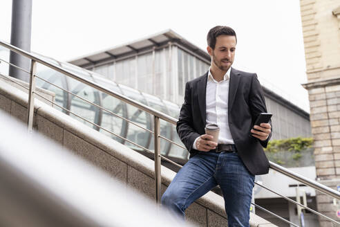 Geschäftsmann mit Kaffee zum Mitnehmen und Mobiltelefon in der Stadt - DIGF08128