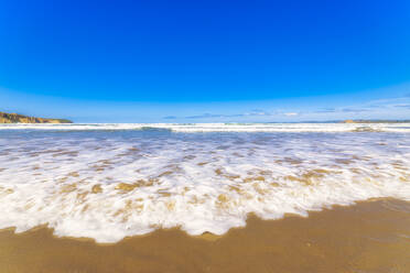 Sea waves rushing towards shore at beach against blue sky in Otago, South Island, New Zealand - SMAF01358