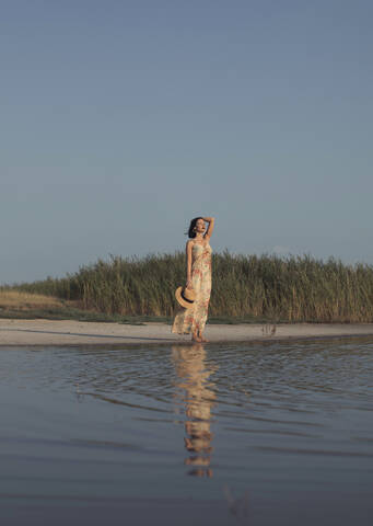 Schöne Frau im Sommerkleid an einem See stehend, lizenzfreies Stockfoto