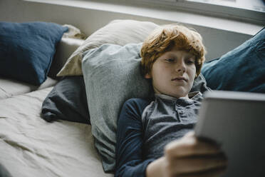 Portrait of redheaded boy lying on couch using digital tablet - KNSF06248