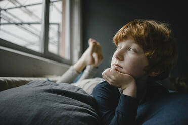 Porträt eines rothaarigen Jungen, der auf einer Couch liegt und aus dem Fenster schaut - KNSF06253