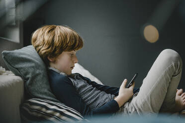 Redheaded boy lying on couch looking at cell phone - KNSF06254