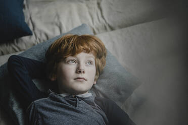 Porträt eines rothaarigen Jungen, der auf einer Couch liegt und in die Ferne schaut - KNSF06259