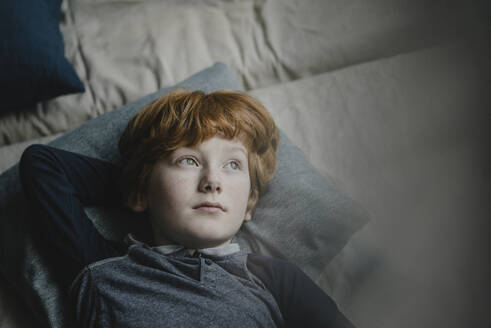 Portrait of redheaded boy lying on couch looking at distance - KNSF06259