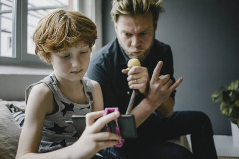 Vater und Sohn mit Smartphone und Mikrofon zu Hause, lizenzfreies Stockfoto