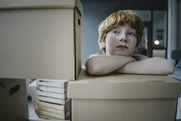 Portrait of redheaded boy leaning on cardboard box - KNSF06273