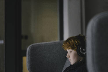 Profil eines rothaarigen Jungen mit Kopfhörern auf einem Ohrensessel - KNSF06285