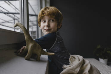 Porträt eines rothaarigen Jungen, der sich abends an die Fensterbank lehnt - KNSF06288
