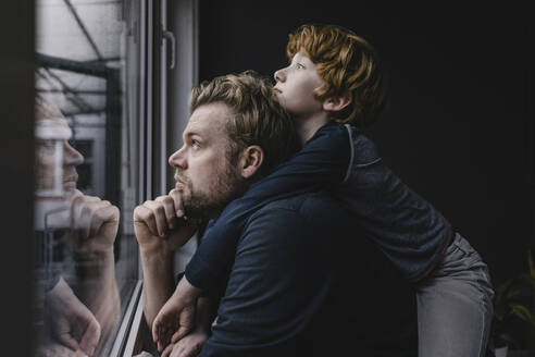 Father and son looking out of window on rainy day - KNSF06297