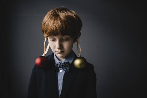 Portrait of redheaded boy wearing bow tie and Christmas baubles - KNSF06303