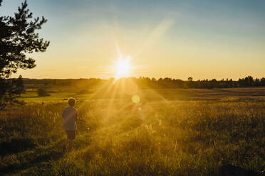 Rückansicht eines auf einem Feld spielenden Jungen gegen den Himmel bei Sonnenuntergang, Polen - MJF02428