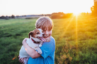 Fröhlicher Junge mit Hund auf einem Feld an einem sonnigen Tag, Polen - MJF02433