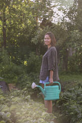 Lächelnde junge Frau mit Gießkanne im Garten - KNTF03046