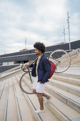 Stilvoller Mann mit Fahrrad auf einer Treppe in der Stadt - AFVF03844